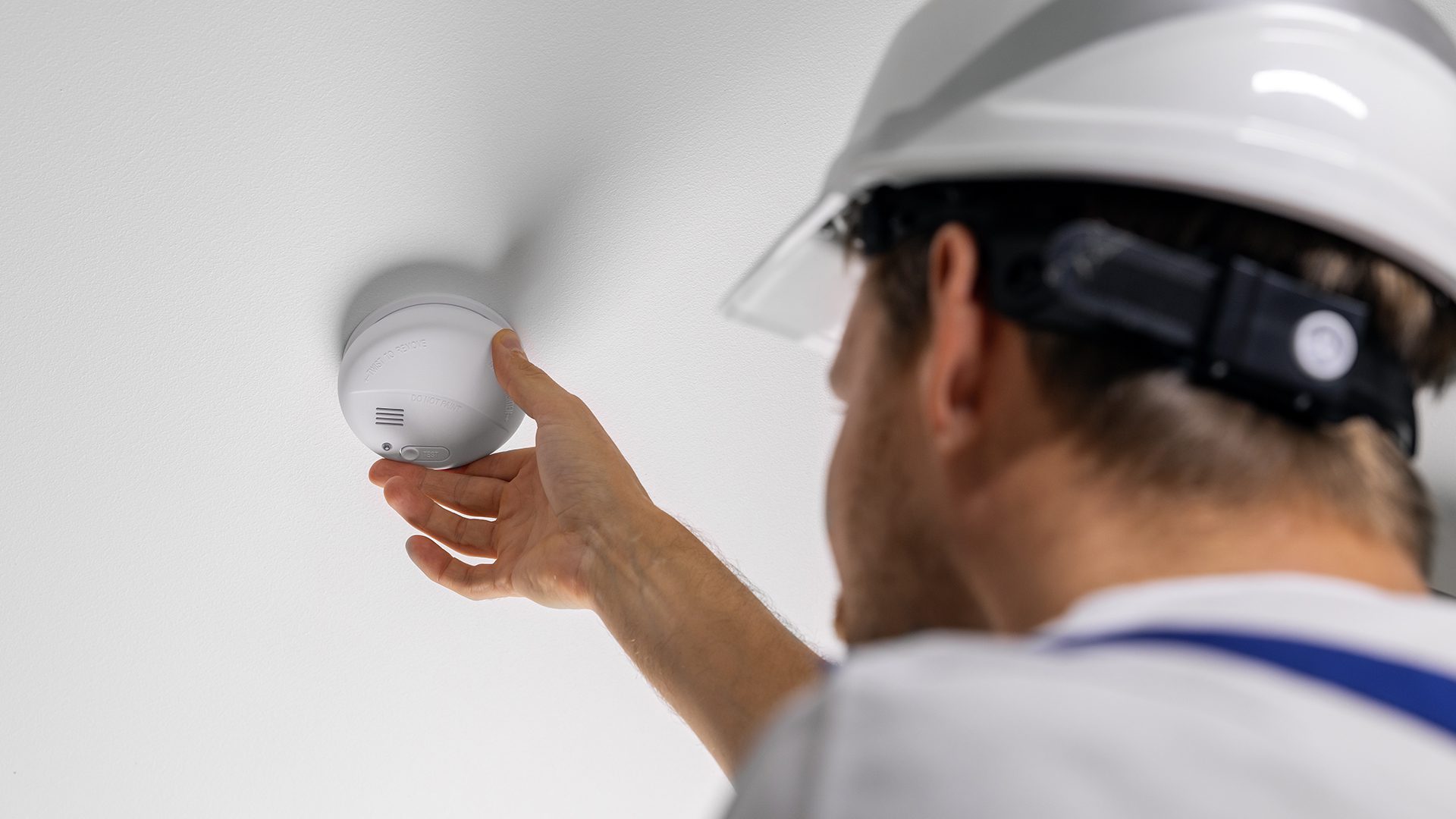 A man in white hard hat pointing to the smoke detector.